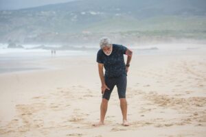 tired elderly man standing on the beach sand